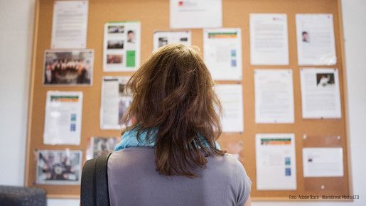 Frau steht vor einer Wandzeitung und liest Aushänge