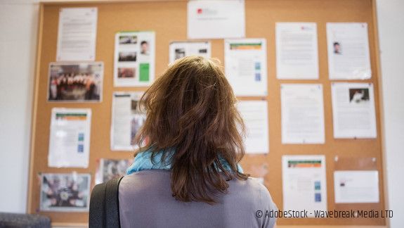 Frau steht vor Aushängen und liest