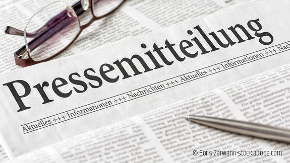 Zeitung mit der Überschrift Pressemitteilung mit Brille und Kuli